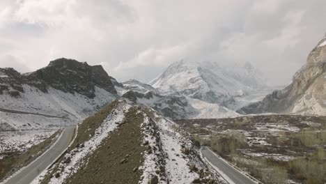 Elevación-Aérea-Junto-A-Una-Carretera-Vacía-Para-Revelar-Una-Montaña-Cubierta-De-Nieve-En-El-Fondo-Del-Valle-De-Hunza