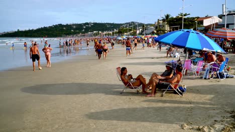 Dolly-Von-Menschen,-Die-Sich-Im-Sand-Unter-Sonnenschirmen-In-Der-Nähe-Der-Küste-An-Den-Stränden-Von-Bombas-Und-Bombinhas,-Brasilien,-Entspannen