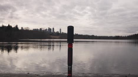 360-camera-on-monopod-on-the-edge-of-a-lake-capturing-landscape-photography-videography-of-water-clouds-trees-sky