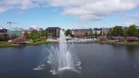 Upward-moving-aerial-flying-over-lille-Lungegård-water-with-fountain---Revealing-festplassen-with-covid-testing-station-and-city-centre