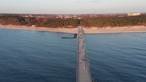 Luftaufnahme:-Menschen,-Die-Am-Abend-Während-Der-Goldenen-Stunde-Auf-Dem-Palanga-Pier-In-Richtung-Stadt-Laufen