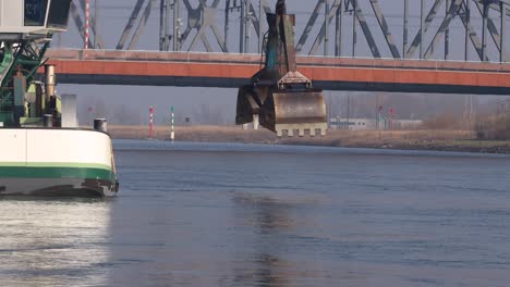 Sumergiendo-Una-Gran-Garra-Industrial-Frente-A-Un-Puente-De-Hierro-Que-Limpia-El-Canal-Del-Río-Ijssel