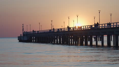 Menschen,-Die-Am-Späten-Abend-Am-Palanga-Pier-Spazieren-Gehen-Und-Angeln,-Während-Die-Sonne-Am-Himmel-Untergeht