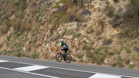 Ciclista-Pasando-Por-La-Carretera-Mientras-La-Cámara-Lo-Sigue-Por-La-Mañana