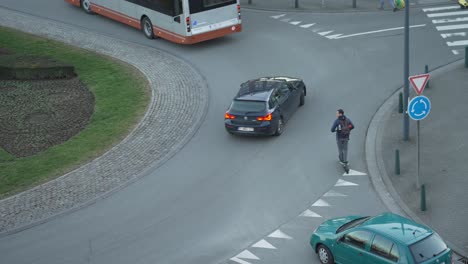 El-Hombre-Que-Viaja-Con-Un-Scooter-Eléctrico-Impone-Su-Lugar-En-La-Rotonda-En-El-Tráfico-De-La-Ciudad,-Tiro-De-Arriba-Hacia-Abajo