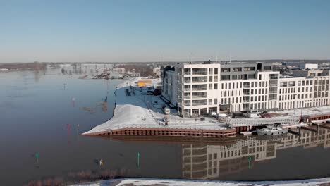 Luftaufnahme-Von-Noorderhaven-Und-Enthüllung-Eines-Zeitgenössischen-Neuen-Luxusapartmentgebäudes-Im-Hellen-Verschneiten-Stadtbild,-Gespiegelt-Im-Hohen-Wasserstand-Im-Freizeithafen-Im-Vordergrund