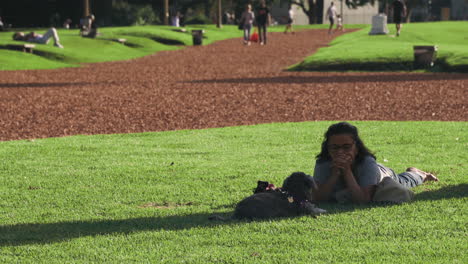 Mujer-Con-Su-Perro-Tirado-En-El-Césped-Del-Parque