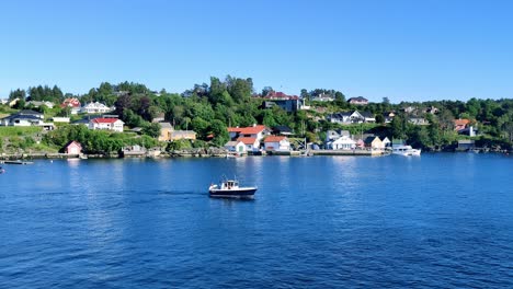 Una-Pequeña-Embarcación-De-Recreo-Targa-Navegando-Alrededor-De-La-Bahía-De-Hjellestad-En-Un-Día-Soleado---Tiro-Estático-Noruega-Con-Casas-Caras-En-Segundo-Plano