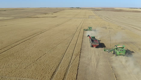 Aerial-following-combines,-tractor-harvesting-wheat-in-Saskatchewan,-Canada