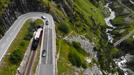 Luftaufnahme:-Dampfzug-Verlässt-Den-Tunnel-Und-Fährt-Eine-Kurvenreiche-Straße-Entlang