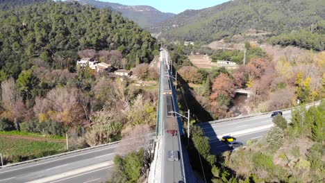 Aerial:-passenger-train-crossing-a-steel-bridge-over-a-main-road-and-mobing-away