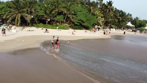 Panorámica-Aérea-A-La-Derecha-De-Dos-Jóvenes-Caminando-En-La-Orilla-De-La-Arena-Cerca-De-Las-Olas-Del-Mar-Y-La-Selva-Tropical-De-Palmeras,-Playa-De-Mirissa,-Sri-Lanka