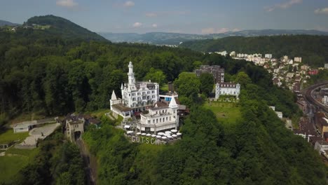 órbita-Aérea-Del-Lujoso-Hotel-Chateau-Gutsch-En-La-Cima-De-Una-Colina-Rodeada-De-Un-Denso-Bosque,-Cerca-Del-Casco-Antiguo-De-Lucerna-Durante-El-Día,-Suiza