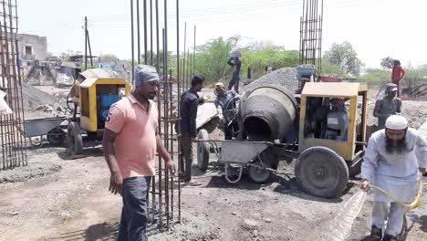 Old-dirty-concrete-mixer-near-sand-heap-at-small-construction-site