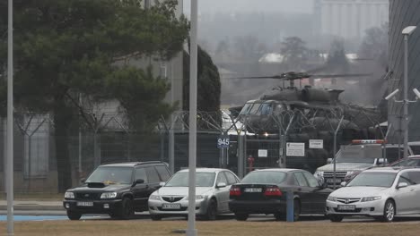 Ein-Militärhubschrauber-Rollt-über-Einen-Flugplatz,-Zivilautos-Parken-Vor-Dem-Sicherheitszaun-Des-Flughafens