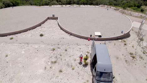 Dos-Hombres-En-Trajes-De-Materiales-Peligrosos-Que-Se-Acercan-A-Un-Depósito-De-Agua-De-Tanque-Doble-Con-Una-Camioneta-De-Trabajo-Estacionada,-Vista-Aérea-Hacia-Abajo,-Toma-De-Seguimiento