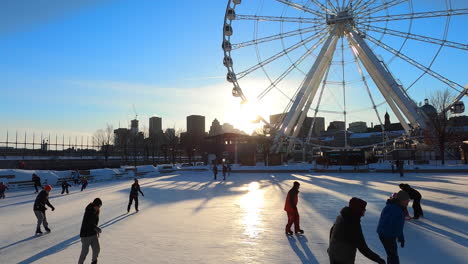 Eislaufbahn-Im-Alten-Hafen-Von-Montreal-Neben-Dem-Großen-Riesenrad,-Menschen-Skater,-Die-Draußen-Winter-Skateaktivitäten-Genießen,-Freizeit,-Winterliches-Touristenattraktionsziel,-Montreal-Gebäude-Im-Hintergrund