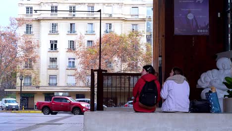 Handheld-of-the-Gabriela-Mistral-cultural-center-GAM,-with-a-couple-of-girls-sitting-and-talking,-Santiago,-Chile