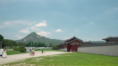 Una-Pareja-Vestida-Con-Hanbok-Y-Otros-Turistas-Entran-Por-La-Puerta-Yongseongmun-Al-Palacio-Gyeongbokgung-Con-La-Cumbre-Del-Monte-Bukhansan-Contra-El-Cielo-Azul-Nublado---Amplio-Paisaje