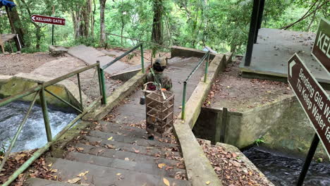 Local-Balinés-Caminando-Por-Escalones-A-Través-De-Un-Pequeño-Puente-Que-Lleva-Una-Jaula-De-Pájaros-Con-Palo-De-Bambú