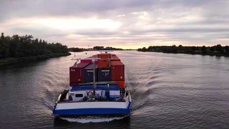 Aerial-Parallax-Around-Forward-Bow-Of-Levante-Cargo-Container-Transport-Ship-Along-Oude-Maas-Against-Sunset-Skies