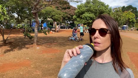 Toma-En-Cámara-Lenta-De-Una-Mujer-Bebiendo-De-Un-Recipiente-De-Agua-En-El-Parque-De-La-Ciudad-De-Brasilia-En-Brasil