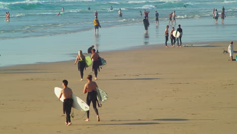 Surfers-Walking-On-Sunny-Beach-Among-With-Other-Vacationists-In-Perranporth,-Cornwall-England