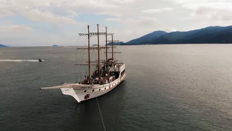 Toma-Aérea-En-órbita-De-Un-Barco-Pirata-Con-Un-Turista-Durante-La-Gira-Oceánica-En-Brasil-Durante-La-Puesta-De-Sol