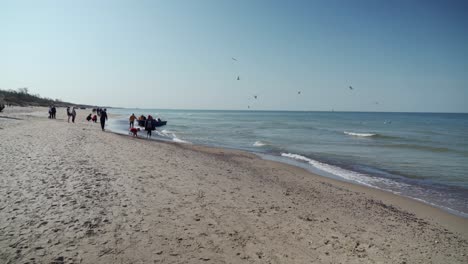 Pescador-Arrastra-El-Bote-A-La-Orilla-En-La-Playa-De-Melnrage-En-Klaipeda-Mientras-La-Gente-Mira