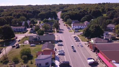 Cars-drive-on-street-in-Grand-Marais,-MI,-on-sunny-day,-forward-aerial