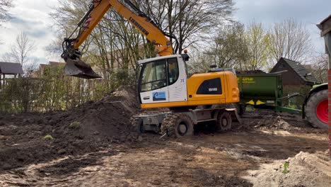 German-Excavator-scoops-sand-and-soil-of-on-construction-site,loading-in-dump-truck-with-tractor