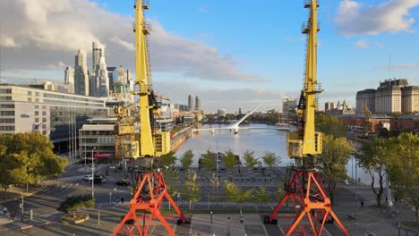 Filmischer-Luftflug-Zwischen-Zwei-Alten-Hafenkränen-Und-Freizügiger-Sicht-Auf-Die-Skyline-Von-Puerto-Madero-Am-Wasser