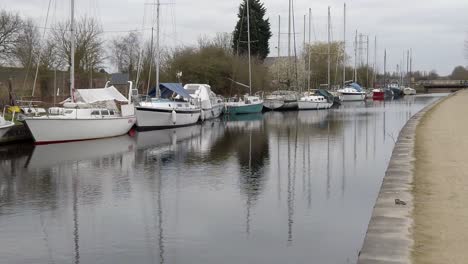 Kleine-Segelboote-Vertäut-Am-Schmalen,-Leeren-Kanalhafen-Auf-Dem-Land