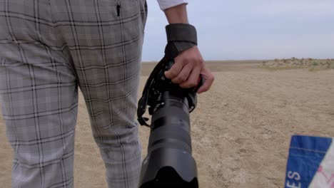 a-photographer-walking-on-the-sand-with-his-camera-in-his-hand,-cloudy-sky