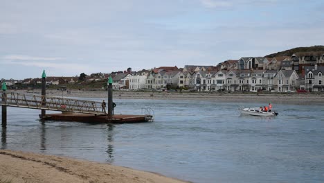 Kleines-Boot,-Das-An-Zwei-Männern-Vorbeifährt,-Die-Auf-Einer-Metallenen-Stegplattform-Am-Meer-Mit-Blick-Auf-Das-Fischerdorf-Warten