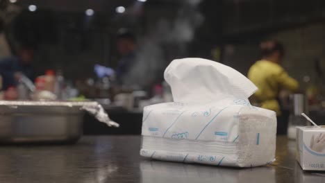 View-of-restaurant-kitchen-with-chefs-working-in-background-with-focus-on-tissues-pack-in-front