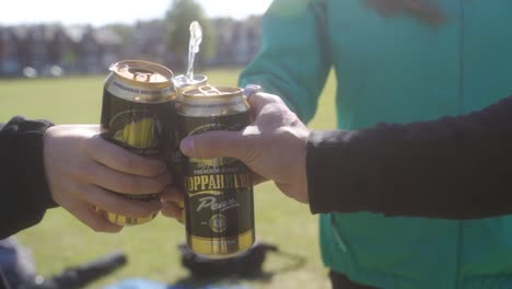 Panning-slow-mo-of-three-people-cheers-drinks-in-Endcliffe-Park,-Sheffield,-England-on-a-sunny-day-in-June