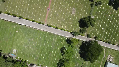 Vista-Aérea-De-Un-Cementerio-Con-Dos-Personas-Que-Avanzan-Por-Un-Camino-Situado-En-Medio-De-Lápidas-Blancas-Dispuestas-En-Filas