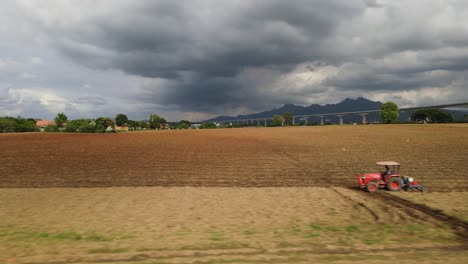 Seguimiento-De-Imágenes-Aéreas-Hacia-La-Izquierda-Que-Revelan-Un-Tractor-Que-Se-Mueve-Y-Deja-Nuevos-Surcos,-Una-Hermosa-Tierra-De-Cultivo-En-Un-Campo-Rural-En-Tailandia,-Sudeste-De-Asia