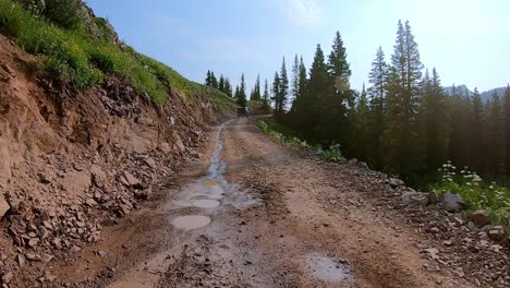 Punto-De-Vista-Siguiendo-Un-Jeep-Conduciendo-Por-Un-Sendero-Circular-Alpino-Cortado-En-La-Ladera,-Pasando-Pinos-En-Las-Montañas-De-San-Jan-Cerca-De-Silverton-Colorado