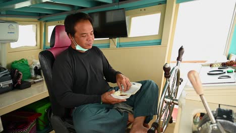 Pilot-of-a-Whale-Watching-boat-eating-his-sticky-rice-and-some-chicken-for-lunch-while-spinning-the-wheel-as-he-follows-the-whale-for-everyone-to-see