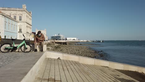 Varón-Anciano-Sentado-En-La-Pared-En-El-Terraplén-En-Lisboa-Con-Cielo-Azul-Claro