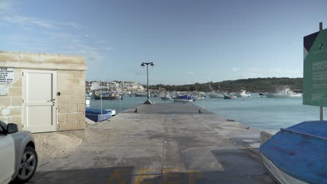 Spaziergang-Auf-Einem-Pier-In-Marsaxlokk-Mit-Wunderschönen-Holzbooten,-Die-In-Der-Bucht-Schwimmen