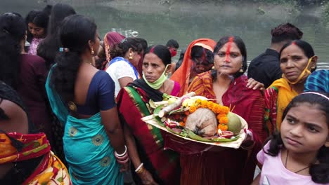 Toma-En-Cámara-Lenta-De-Una-Mujer-De-Pie-Y-Sosteniendo-Artículos-Rituales-Hindúes-Frente-Al-Agua-Del-Río-Ganga-En-Kolkata