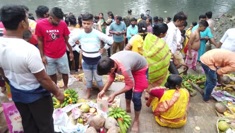 Vista-De-Cerca-De-Personas-Paradas-Frente-Al-Agua-Del-Río-Ganga-Realizando-Rituales-Con-Cestas-De-Cocina-De-Coco-Y-Frutas-Guardadas-En-Los-Escalones-De-Ganga-En-Kolkata