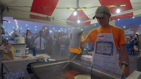 Kleiner-Junge-Gießt-Auf-Einem-Festival-Trichterkuchenteig-In-Eine-Fritteuse