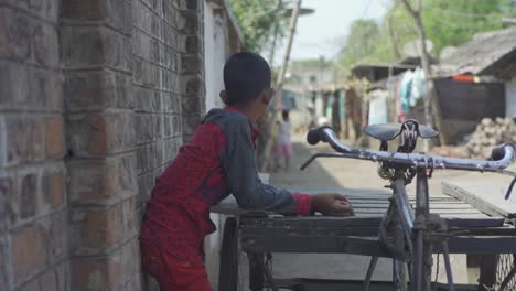 Alone-young-and-poor-Indian-boy-watching-other-children-play-with-friends,-rural-scene