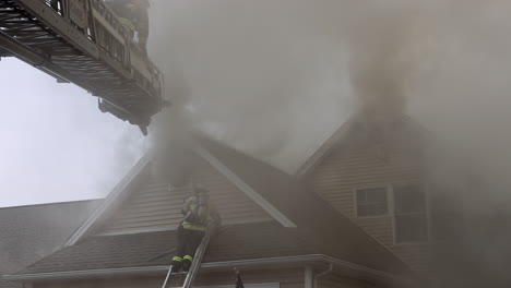 Un-Humo-Espeso-Y-Oscuro-Sale-De-Una-Casa-En-Llamas-Mientras-Los-Bomberos-Usan-Escaleras-Para-Acceder-Al-Techo