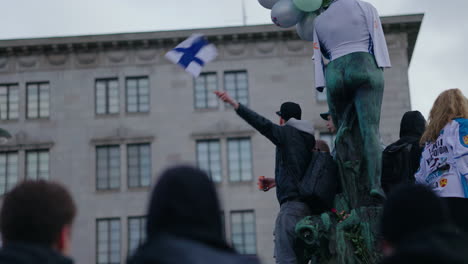 Ventilador-Celebrando-Ondeando-La-Bandera-Finlandesa-En-La-Estatua-De-Havis-Amanda-En-Helsinki,-Celebraciones-Olímpicas-De-Oro-De-Hockey-Sobre-Hielo-En-Finlandia---Toma-En-Cámara-Lenta