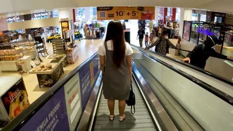 Mujer-Asiática-Usando-Escaleras-Mecánicas-En-Un-Centro-Comercial-En-Yogyakarta-Indonesia,-Vista-Trasera